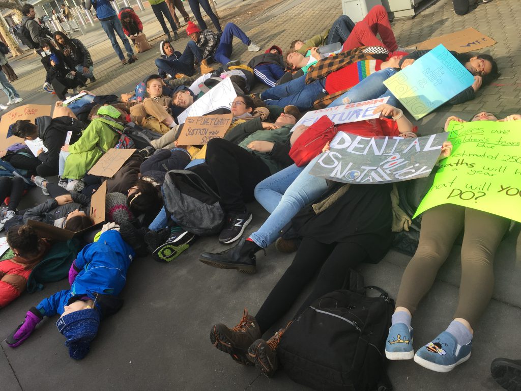 A group of youth stage a "die-in" outside the United Nations Headquarters in New York City in 2019. They are seen laying on the ground, not moving, their signs and placards aroun them.